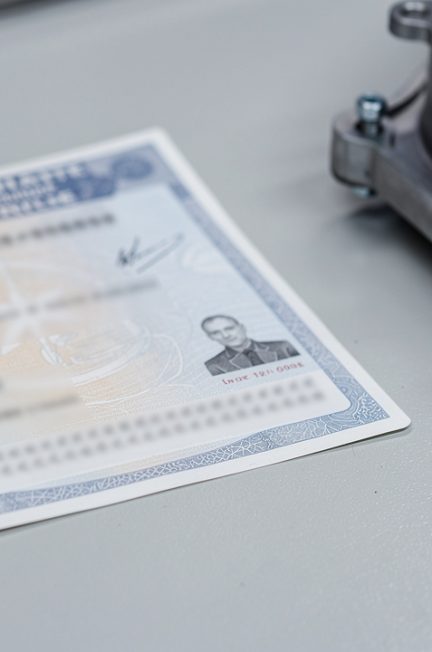 Gros plan réaliste d’un document automobile gris et d’une pièce mécanique métallique disposés sur un établi propre, avec la zone d’identification rendue illisible.