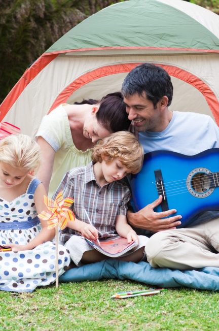Tente de camping familiale montée dans un sous-bois, avec des sacs à dos posés devant l’entrée.